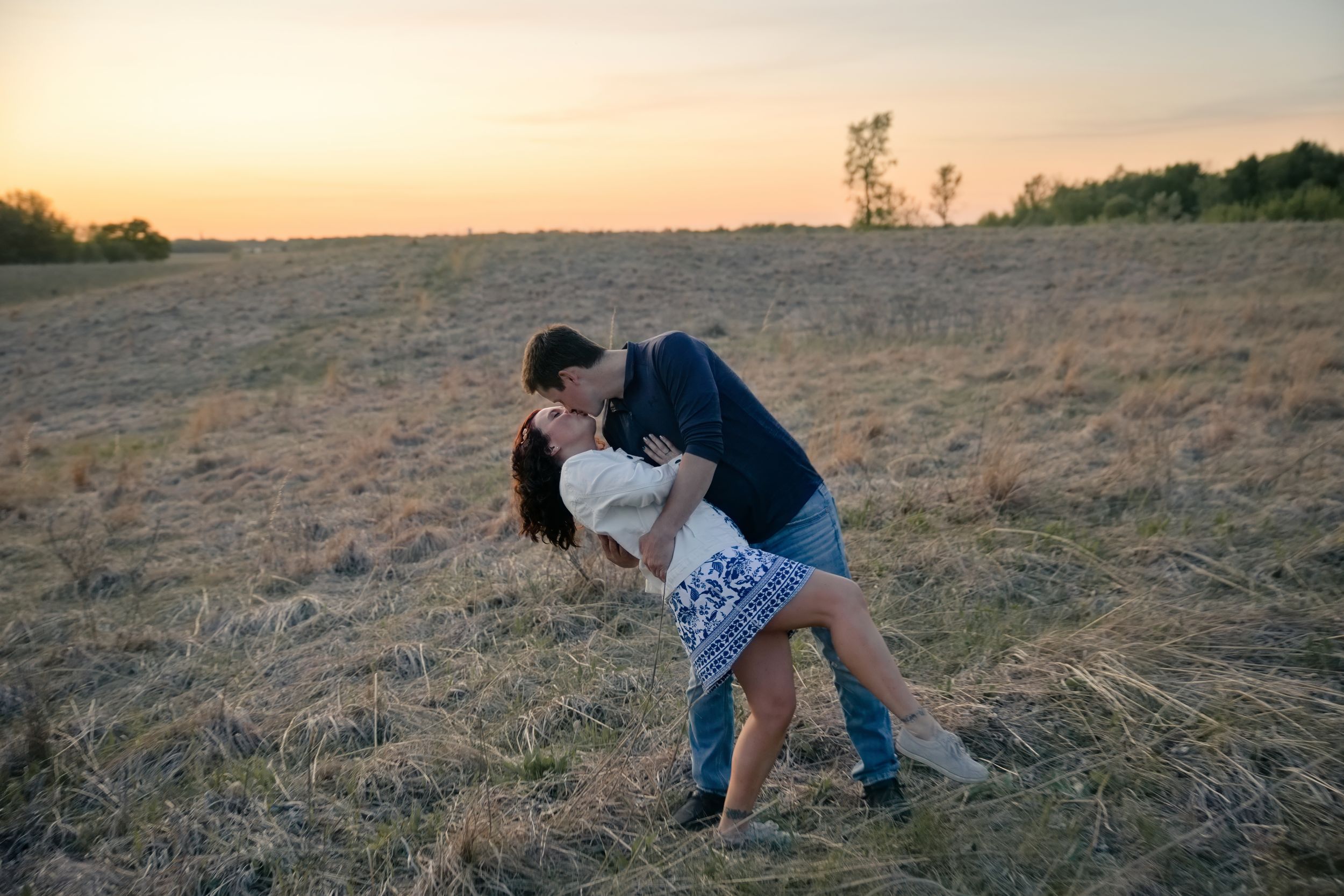 Couple sharing a romantic dip kiss in a golden field at sunset.