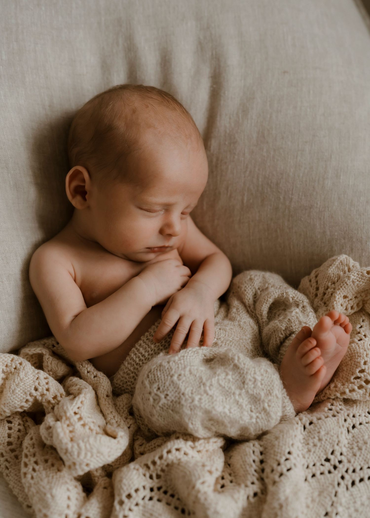 Peaceful newborn baby sleeping on a cream knit blanket with tiny feet visible, perfect for nursery inspiration.