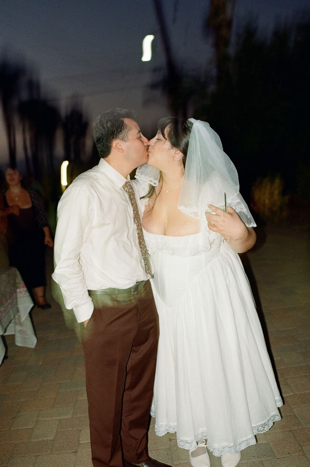 Retro film photo of bride and groom kissing with drinks in hand.