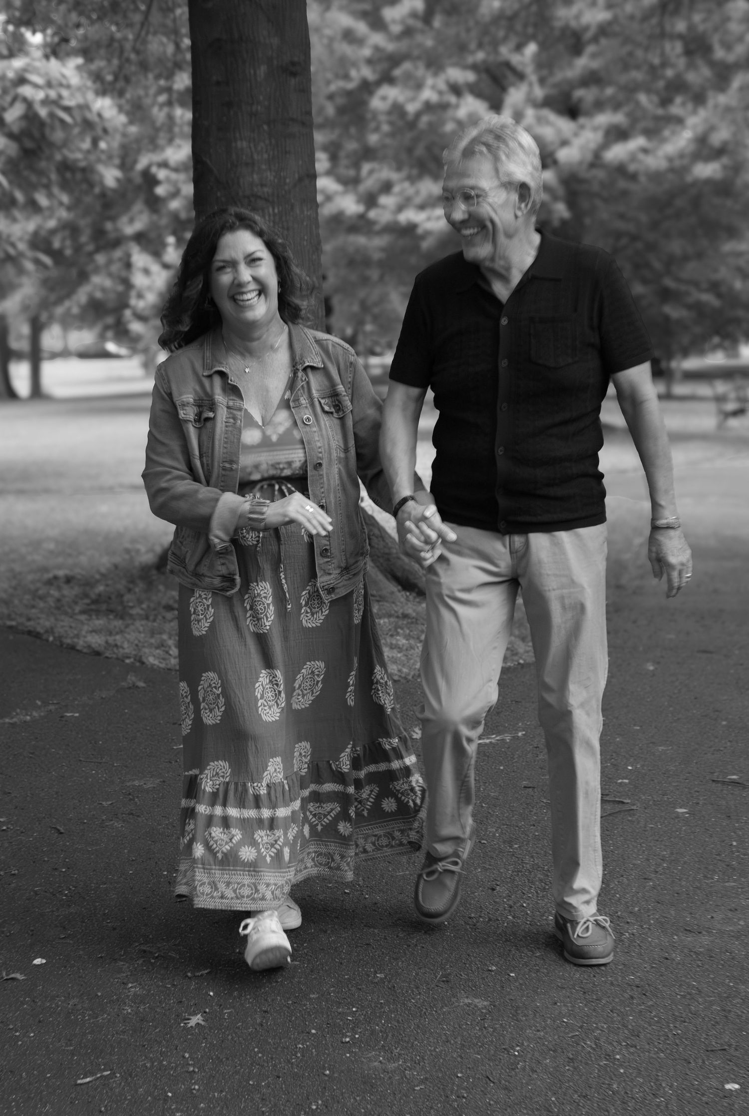 Black and white photo of a smiling couple holding hands while walking together in a park.