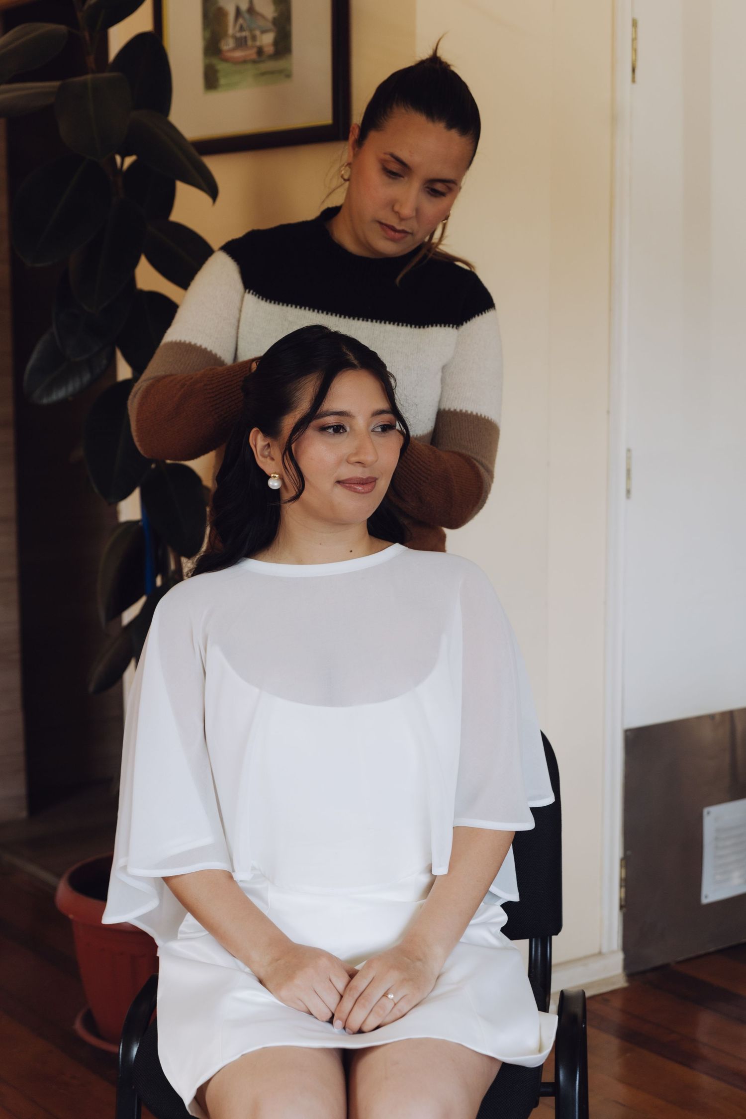 Bride sitting in a white dress getting her hair styled by a hairdresser before her wedding ceremony.