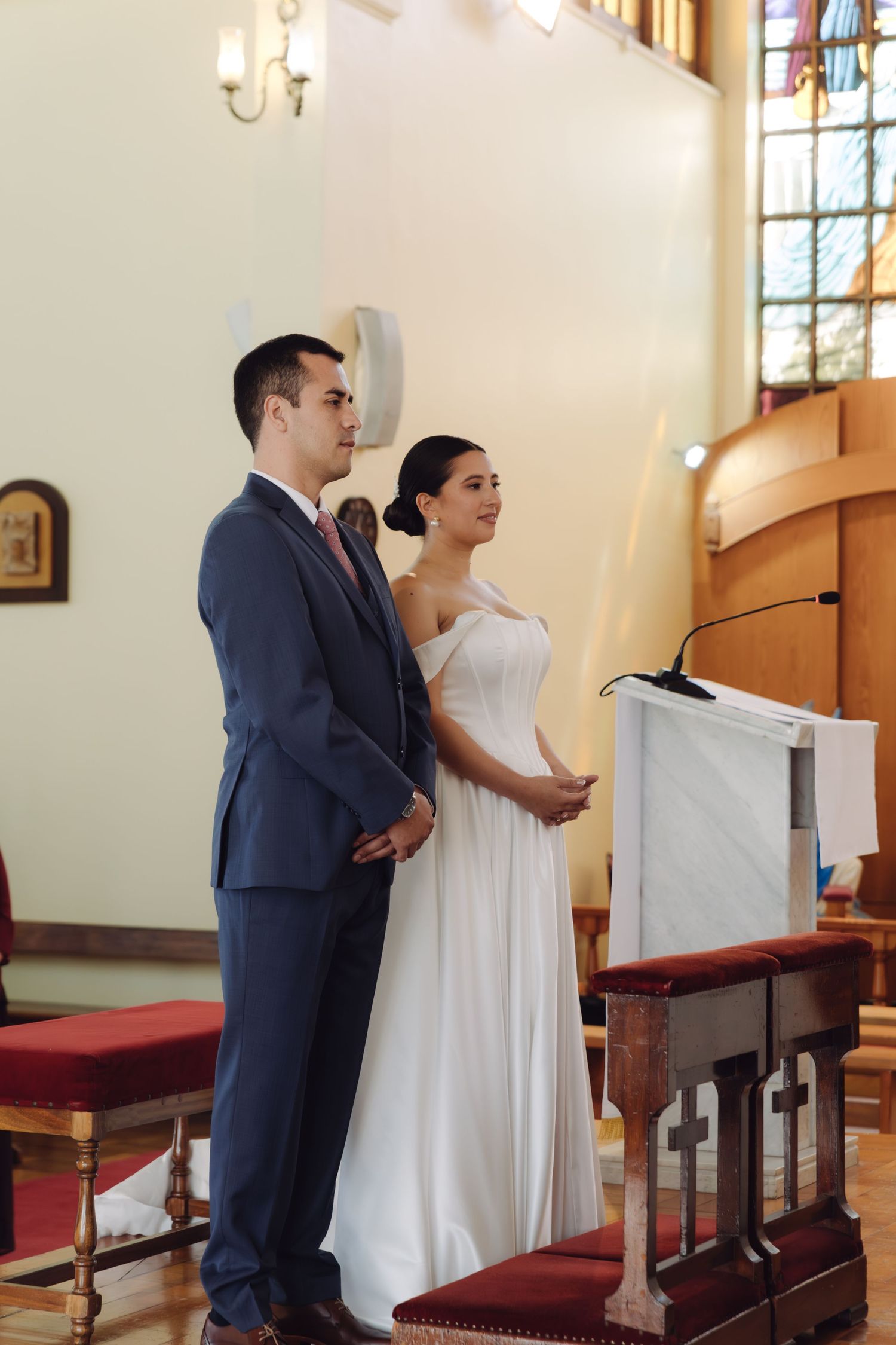 Bride and groom stand attentively at the altar beside a podium during their church wedding ceremony.