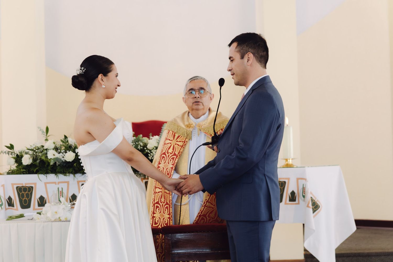 Couple exchanging vows before officiant at elegant church wedding ceremony with floral altar decor.