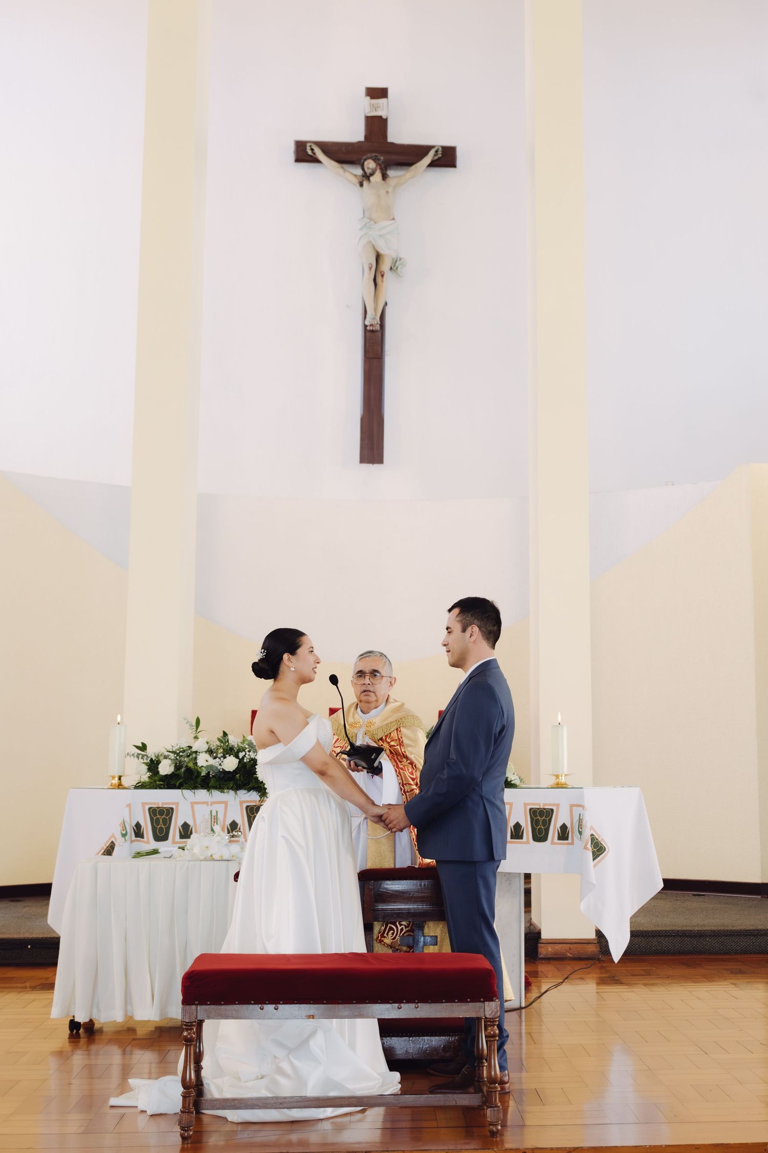 Bride and groom holding hands at altar beneath crucifix during church wedding ceremony.