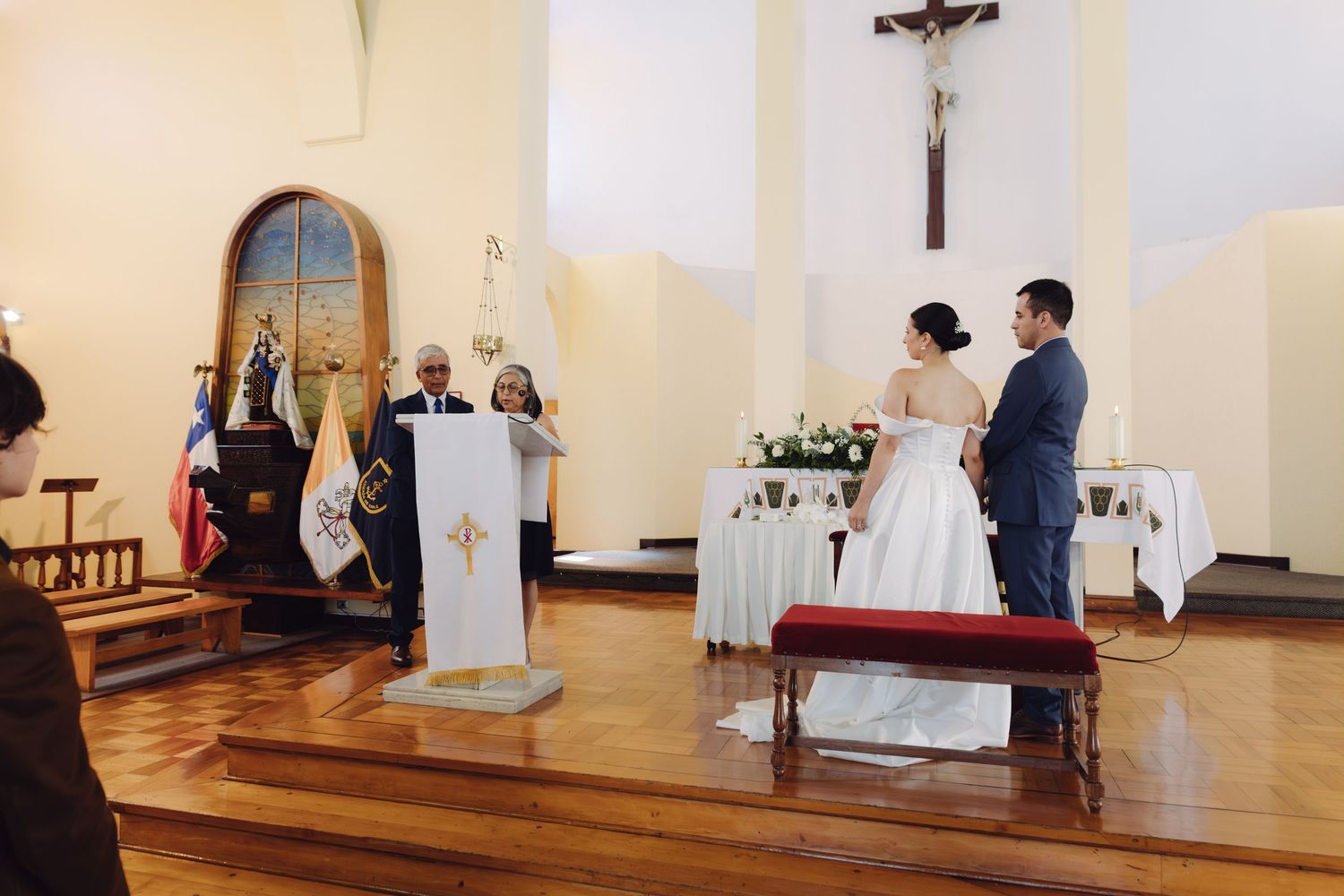 Wide view of Catholic church wedding ceremony with couple at altar and priest reading from podium.