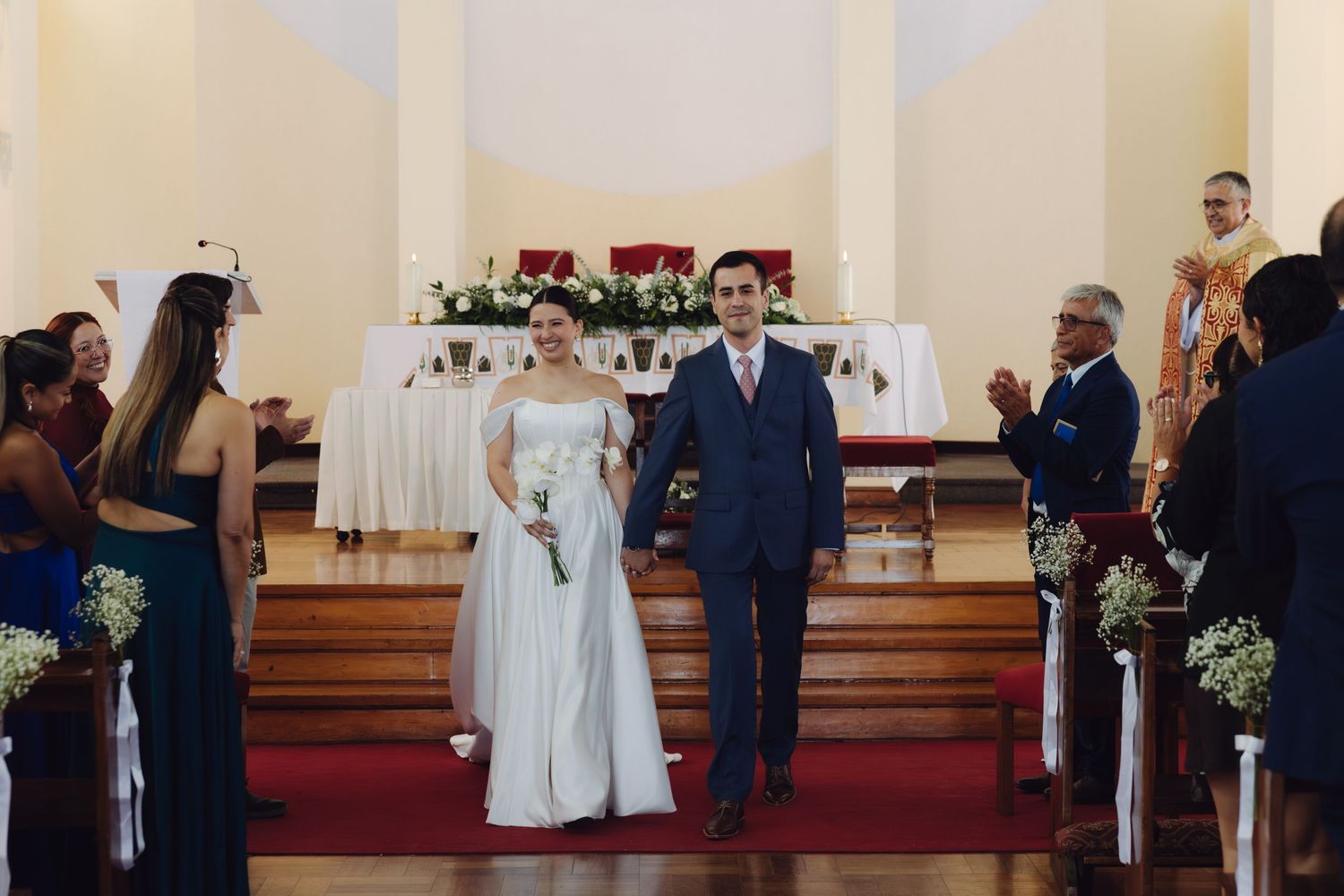 Newlyweds smile as they walk down the aisle of a decorated church.