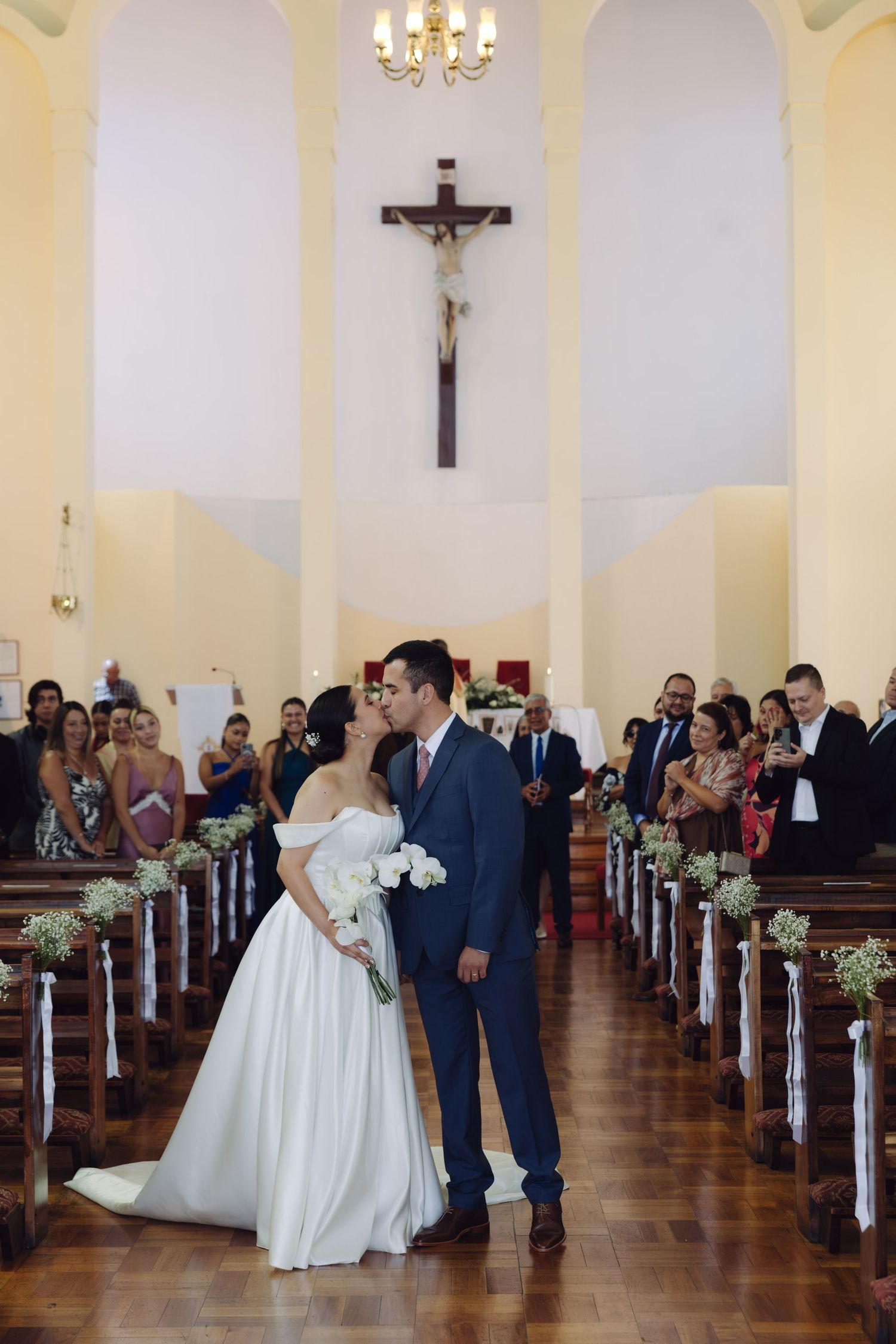 Bride and groom share a kiss in the aisle of a beautiful Catholic church.
