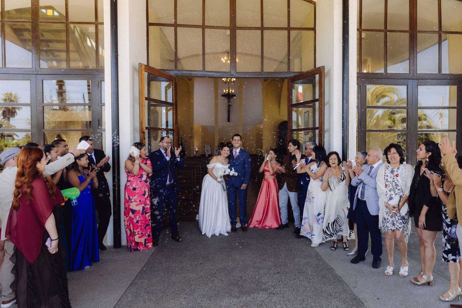 Wedding couple exits church greeted by cheering guests throwing confetti in celebration.