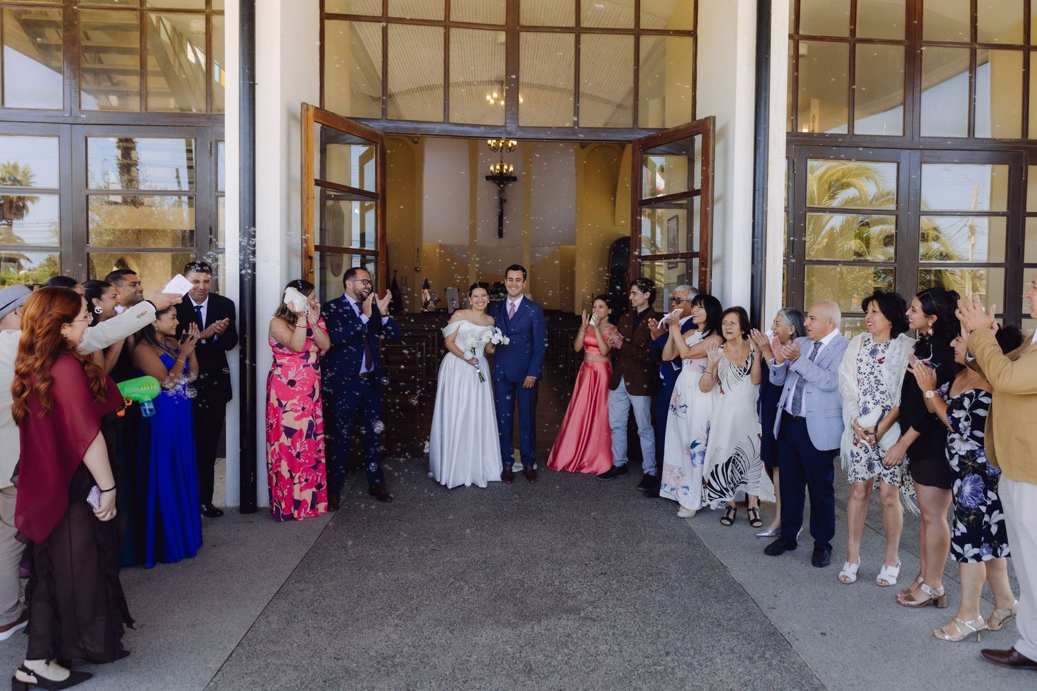 Newlyweds walk out of church entrance as guests celebrate with confetti and applause.