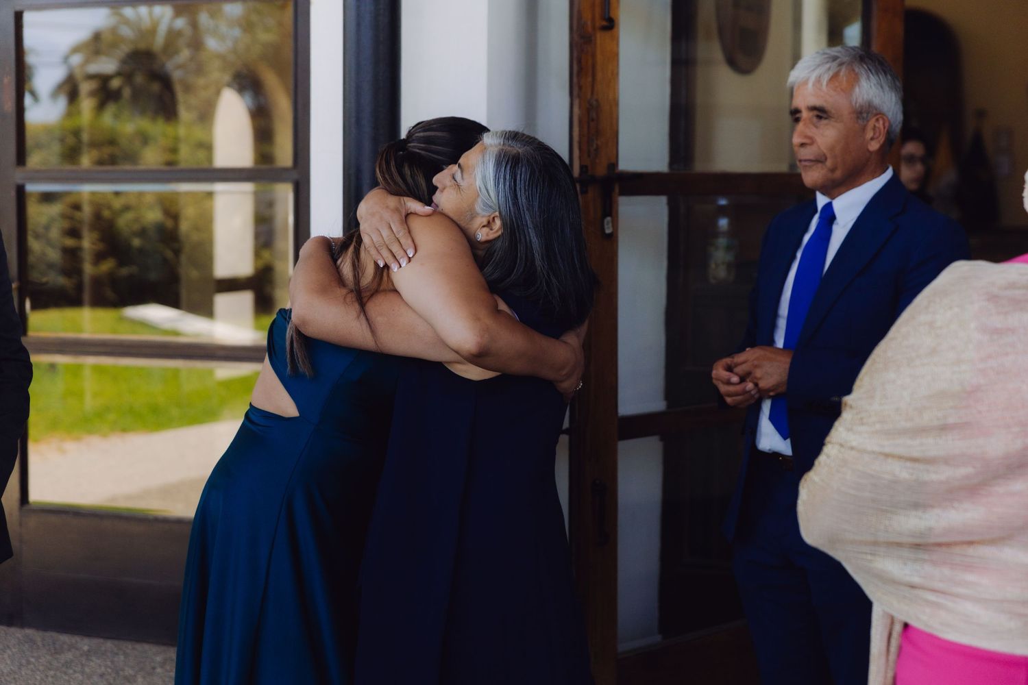 Two women in navy blue dresses sharing an emotional hug at a wedding ceremony.