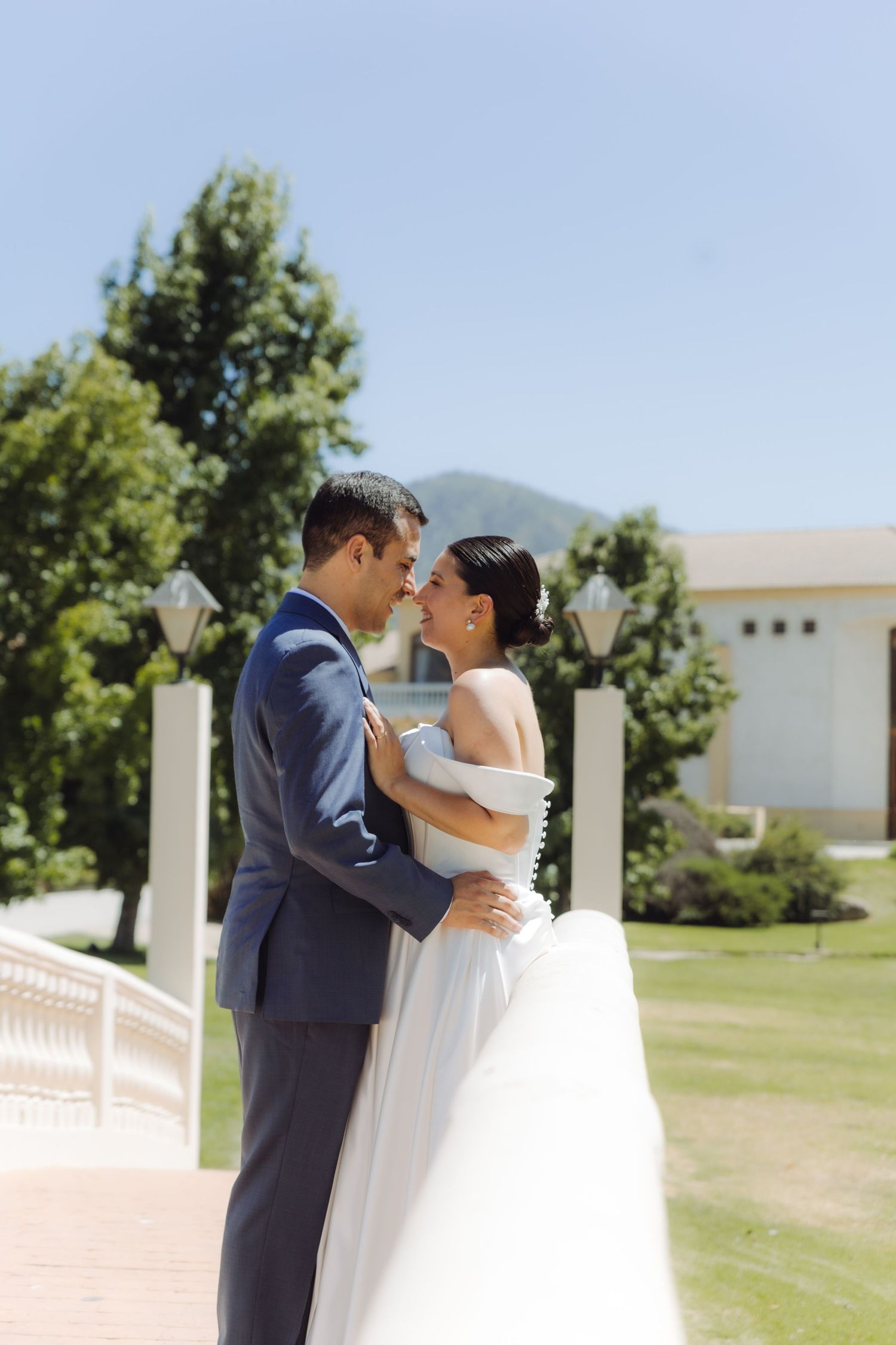 Newlywed couple embracing and gazing into each other's eyes outdoors with mountains and green trees behind them.