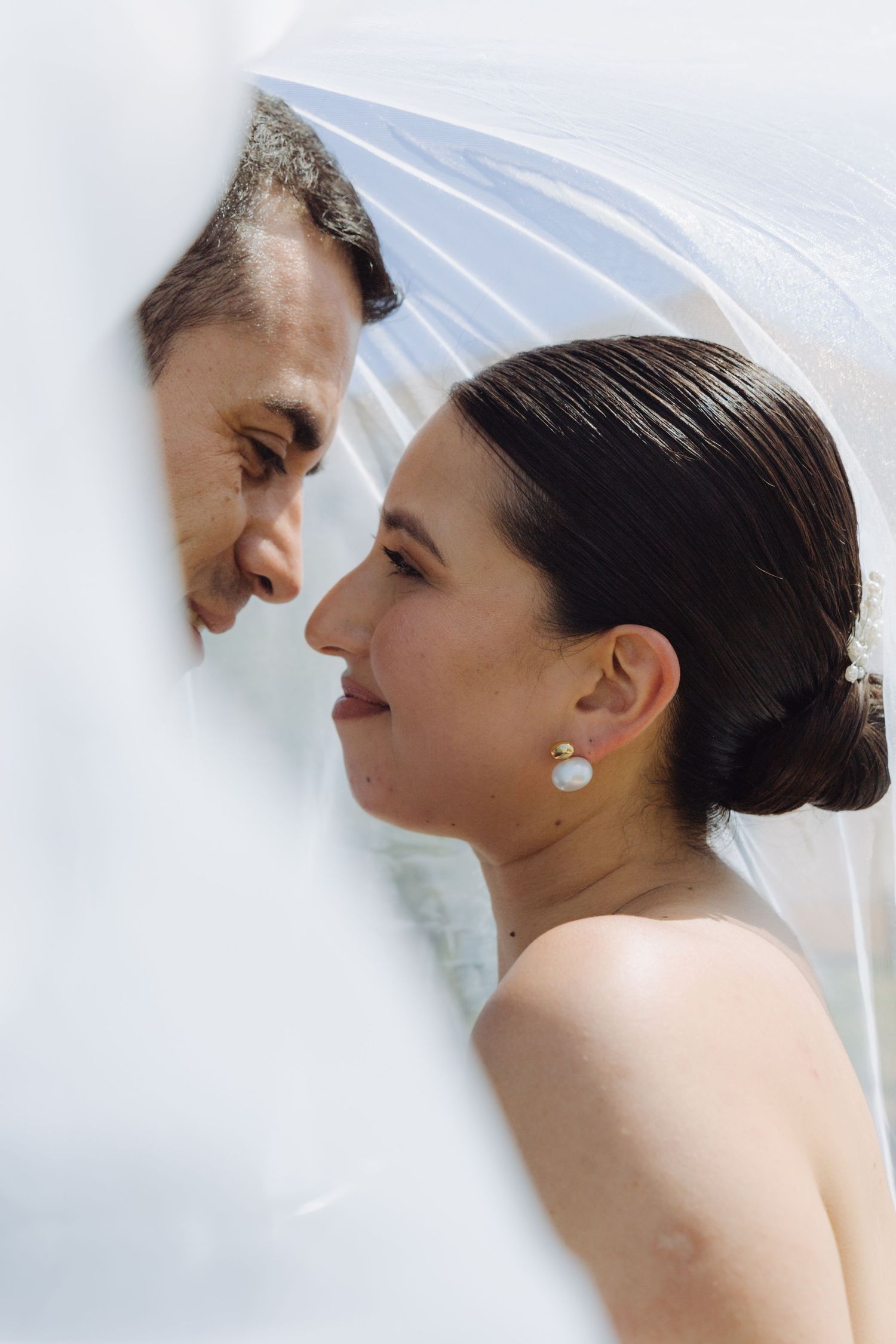 Close-up of bride and groom gazing at each other tenderly under a sheer white wedding veil.