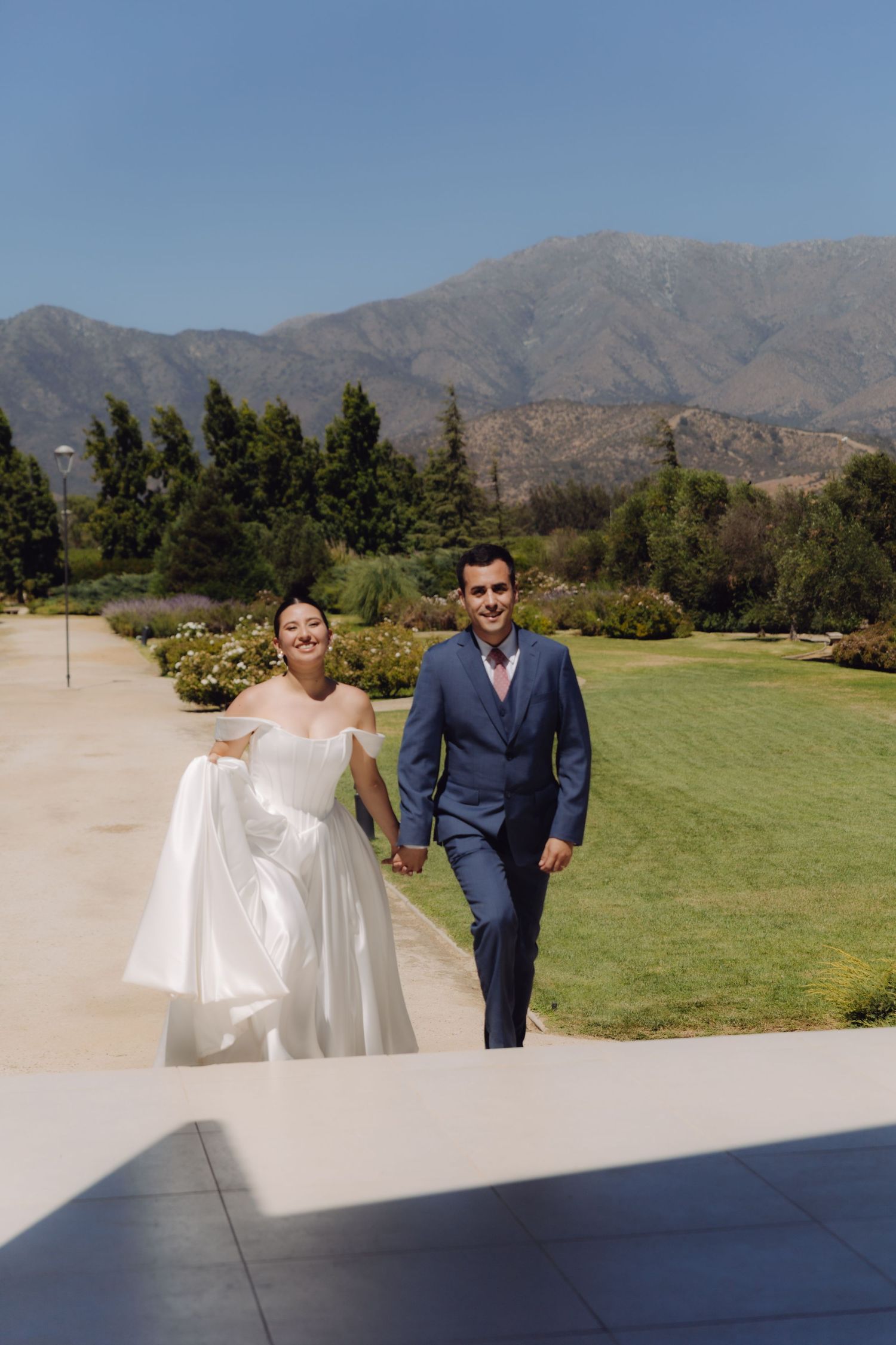 Happy bride and groom walking hand in hand along a path with stunning mountain views behind them.