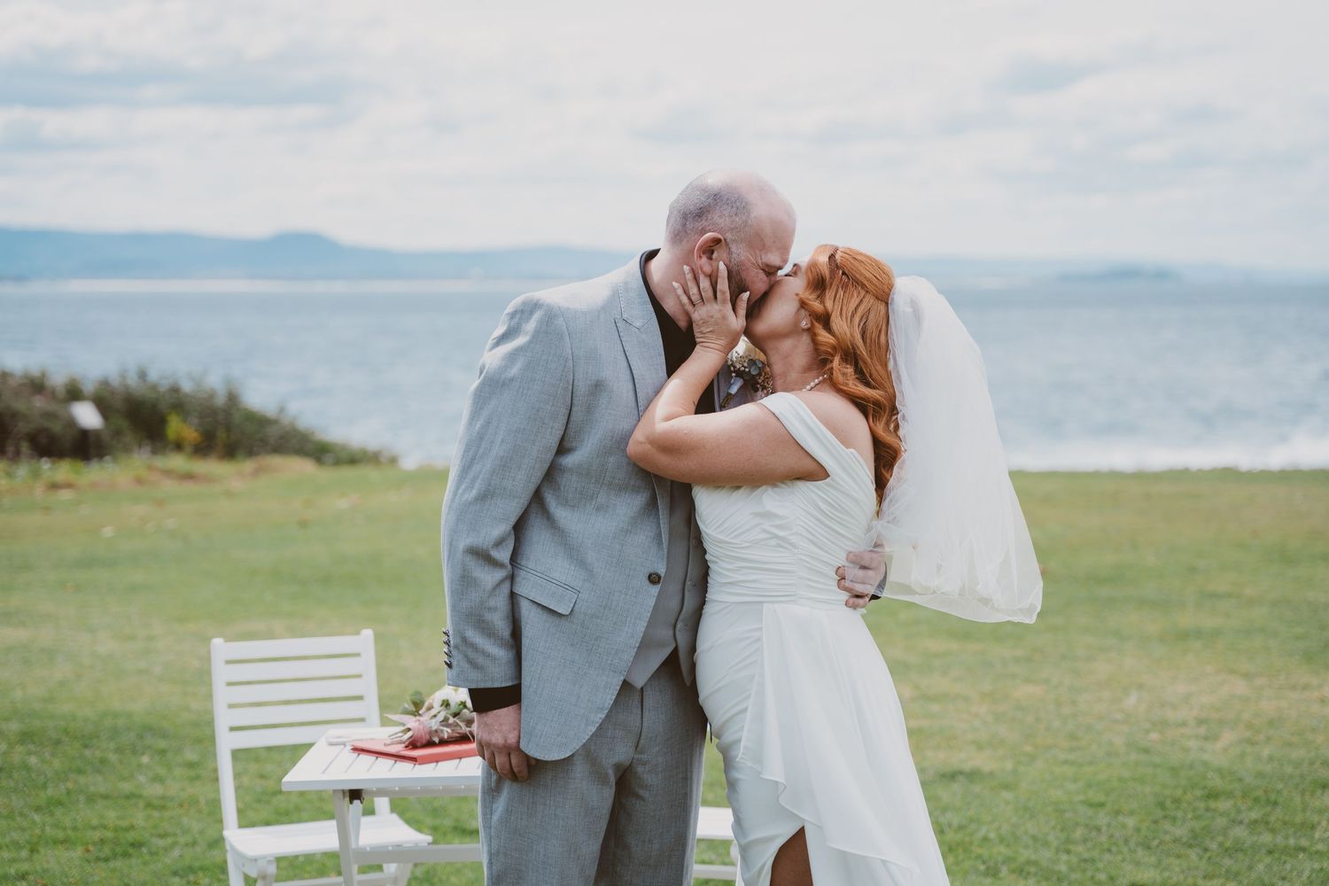Newlyweds share their first kiss on a grassy headland above the water - coastal elopement photography