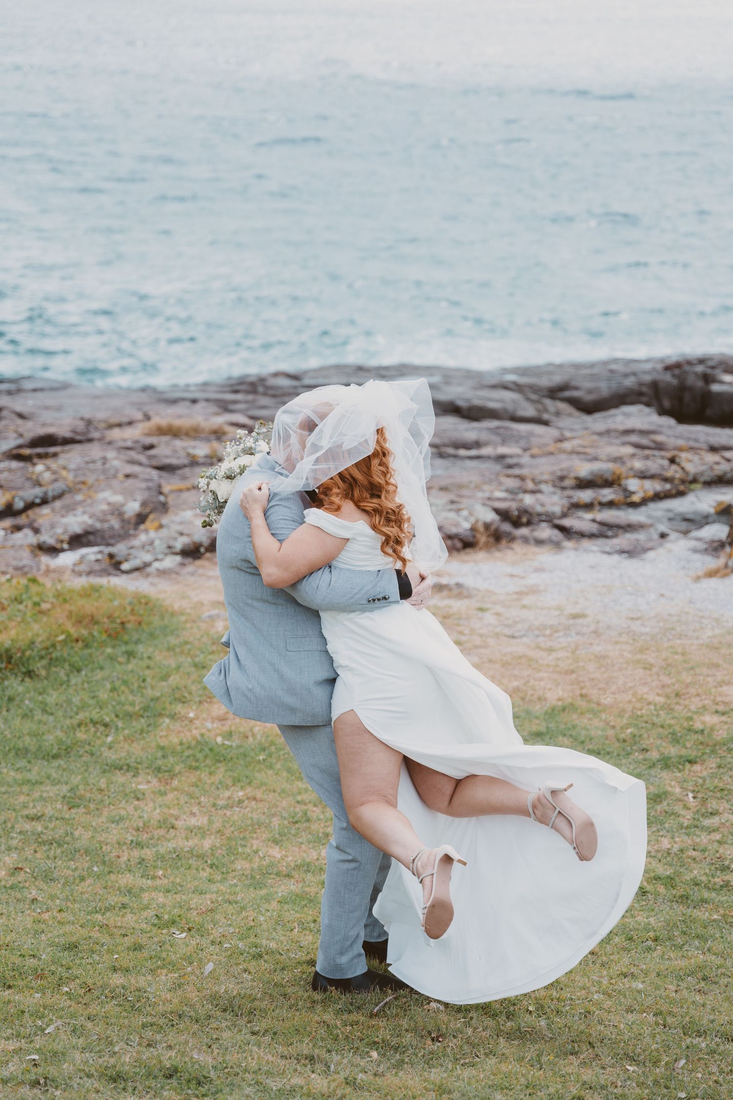 Groom embraces his bride on coastal rocks by the sea - romantic seaside elopement portraits