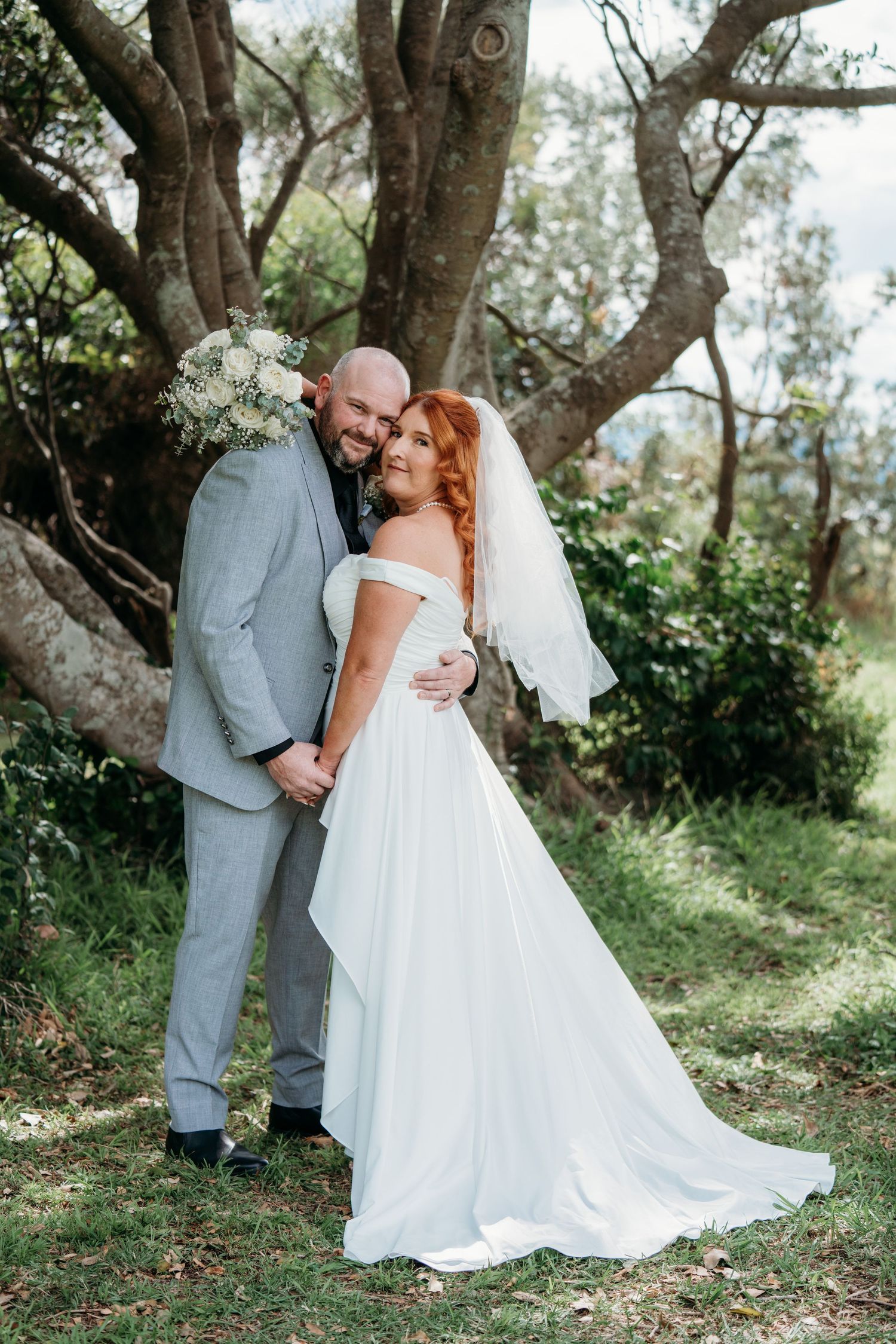 Groom in a grey suit and bride in an off-shoulder dress under twisted trees - coastal elopement couple photos