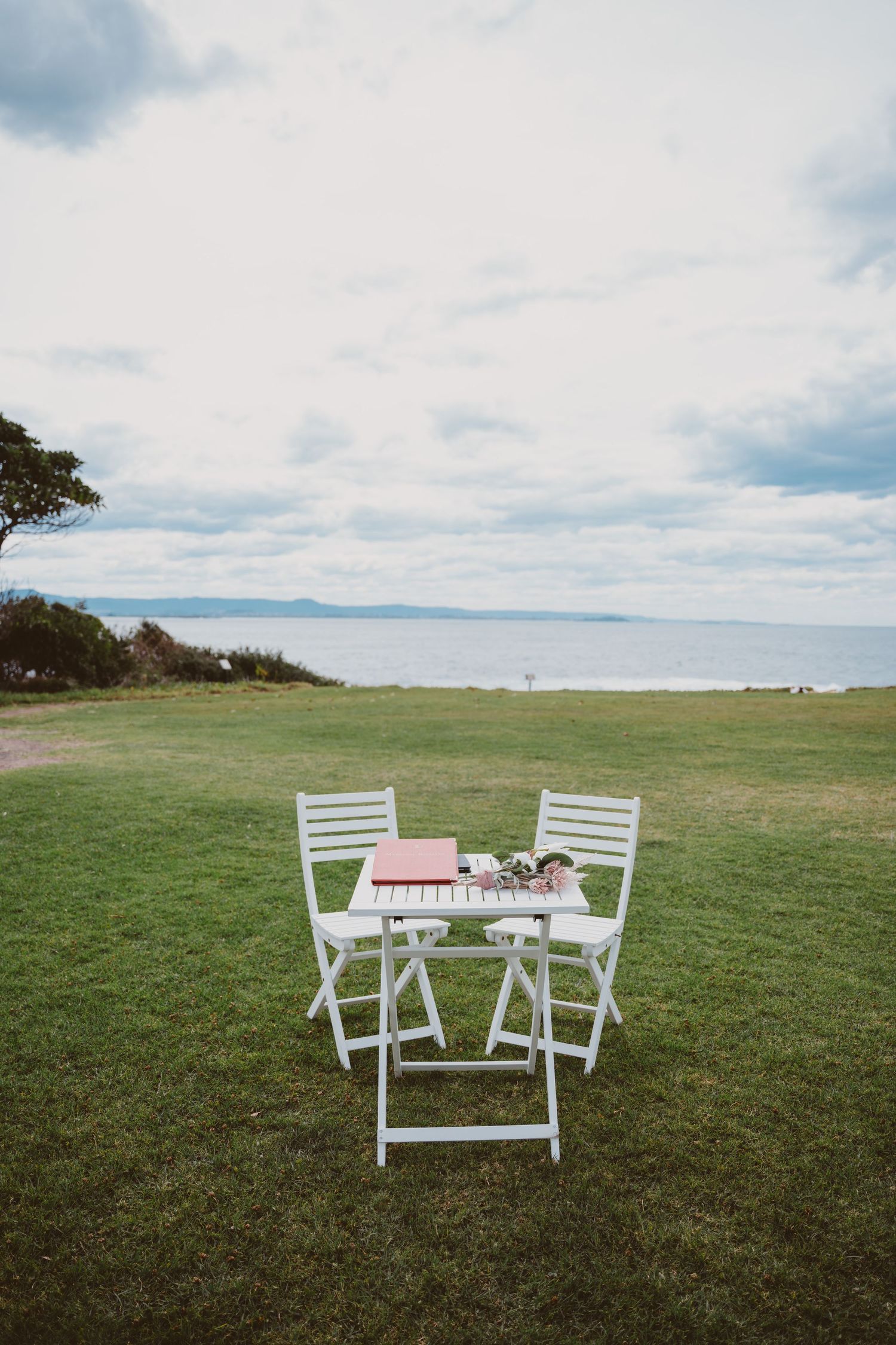 Clifftop lawn with two chairs and a signing table overlooking the ocean - coastal elopement ceremony setup