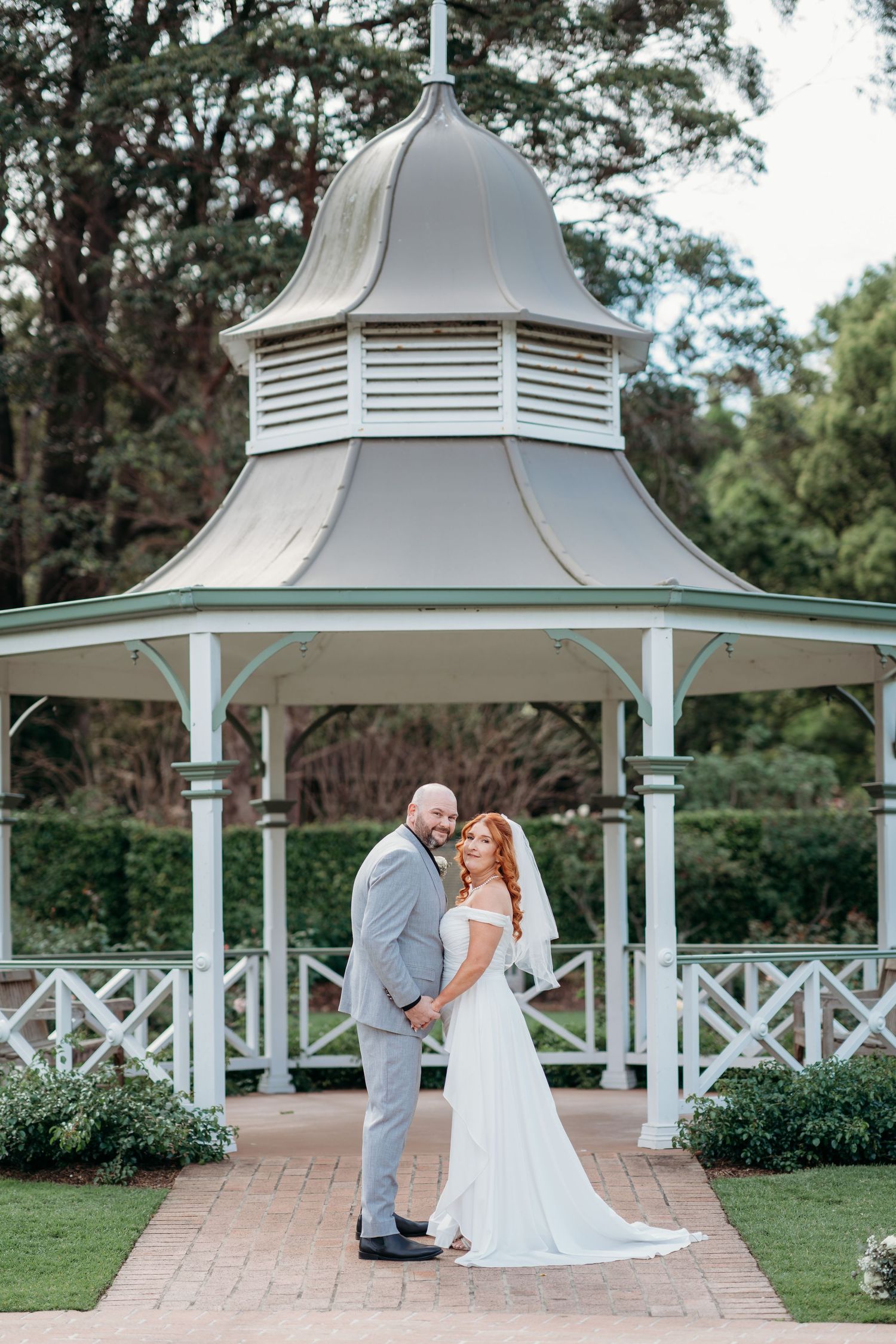 Newlyweds under a white rotunda surrounded by greenery - garden elopement photography
