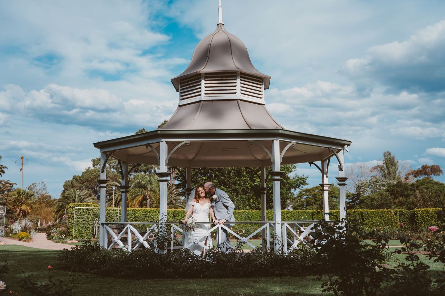 Couple in front of a garden gazebo under a bright blue sky - outdoor elopement portraits