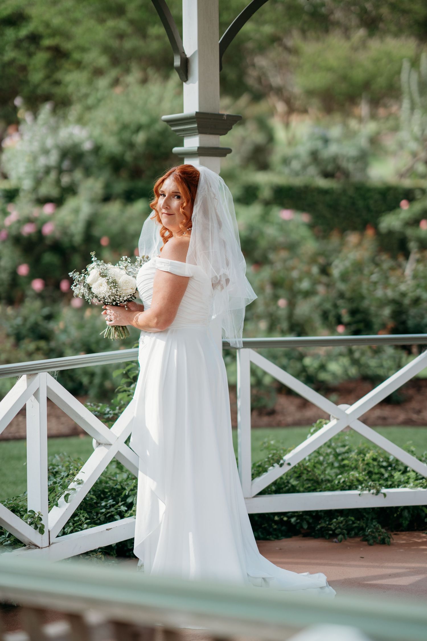 Bride with bouquet leans on a white railing in a garden - elopement bridal portrait