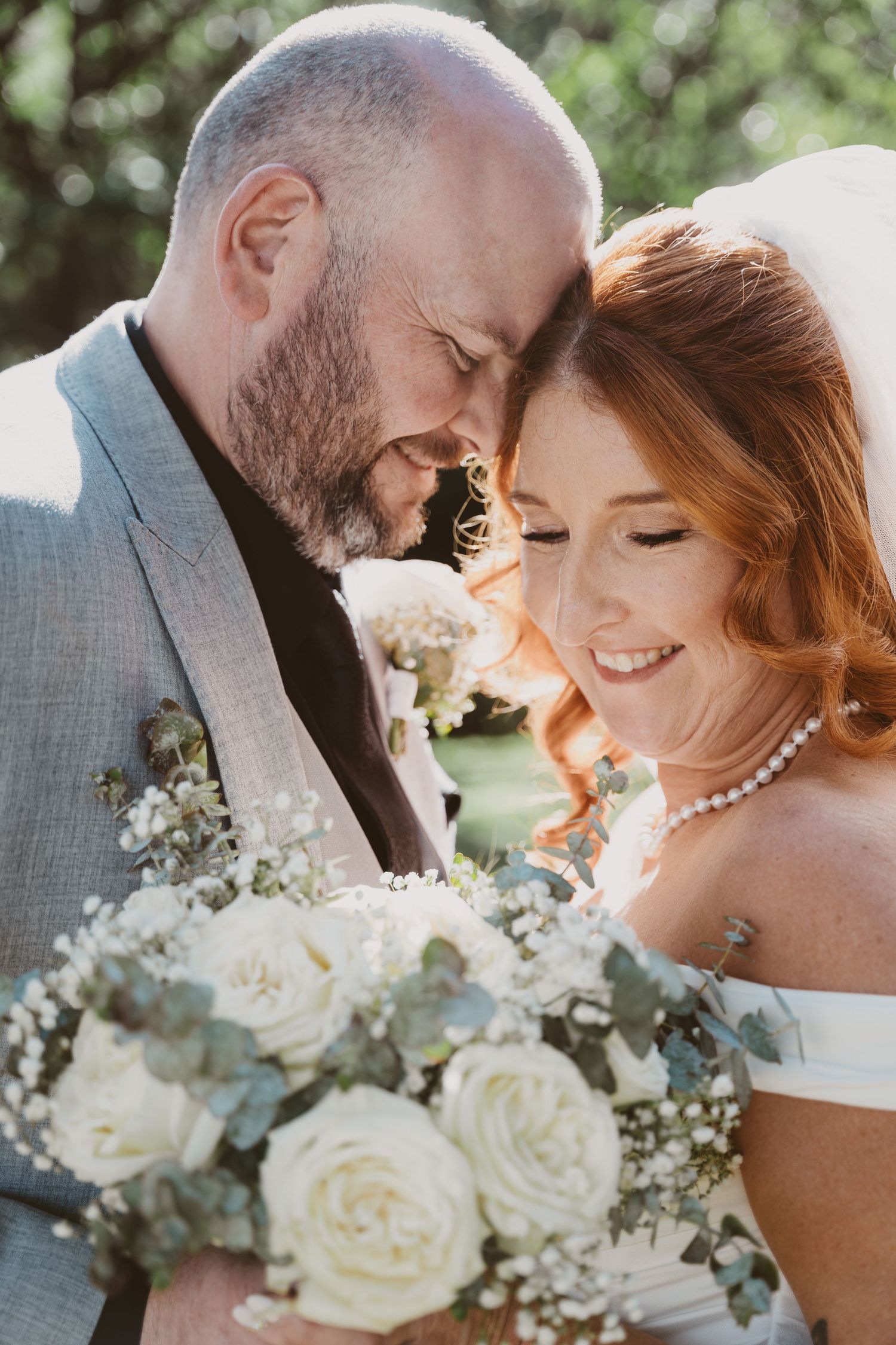 Smiling bride with pearl necklace leans on her groom - intimate close-up elopement portrait