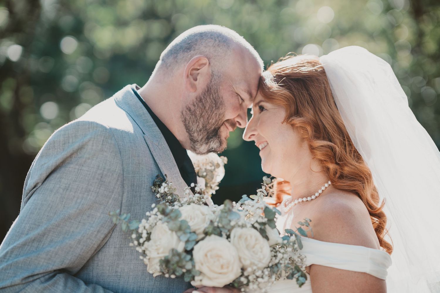 Bride and groom touch foreheads holding a white bouquet - romantic elopement couple photography