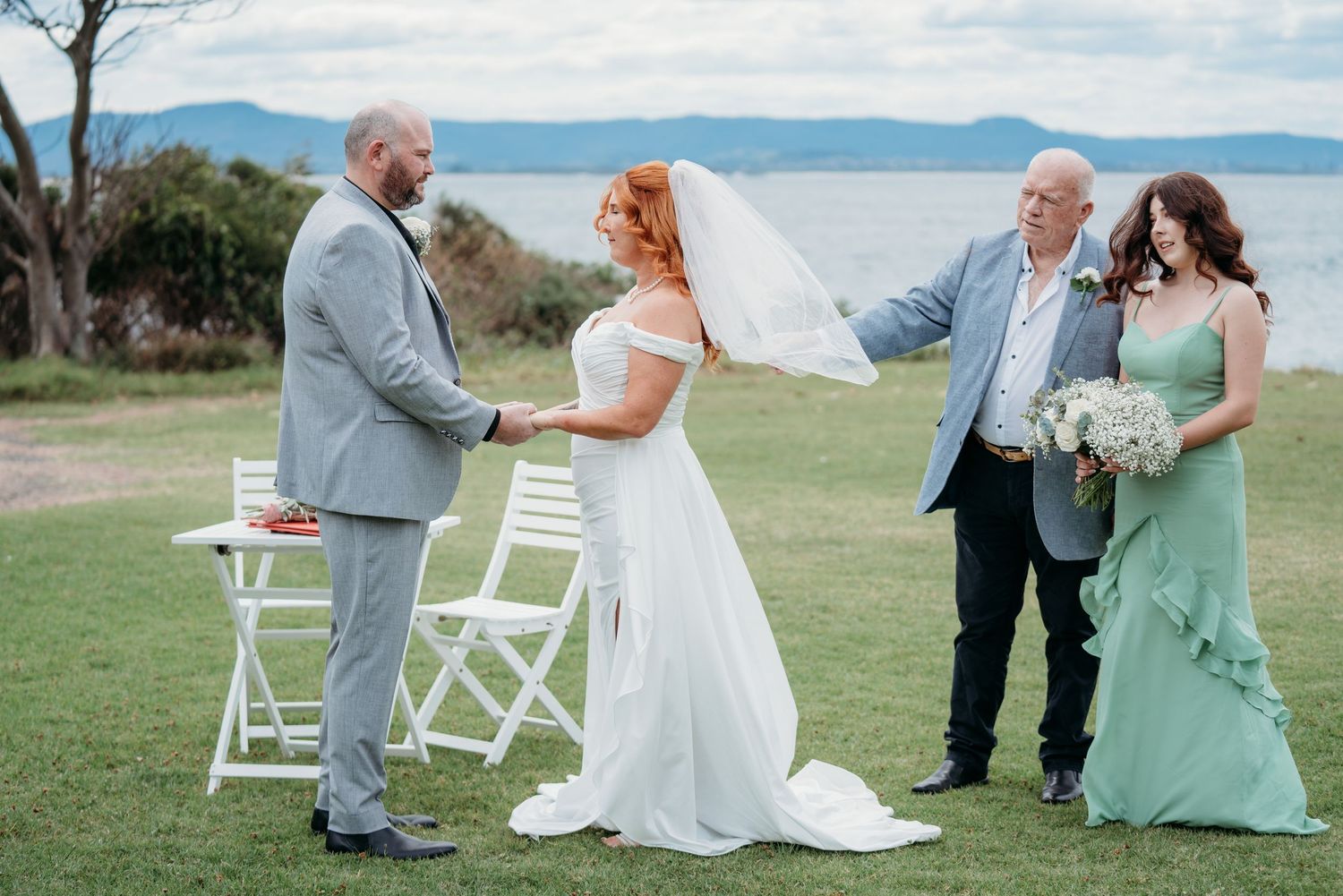 Bride and groom exchange vows with the celebrant on a seaside lawn - intimate coastal elopement, Illawarra style