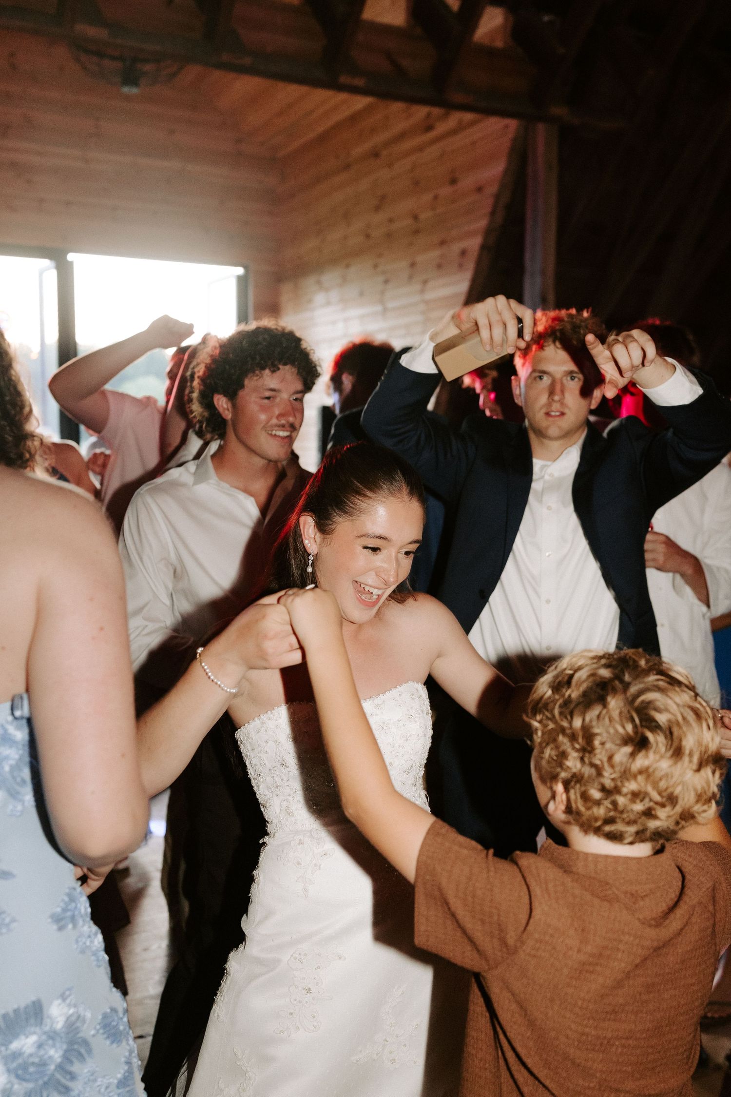 Black and white photo of guests dancing at a wedding reception inside a rustic barn venue.