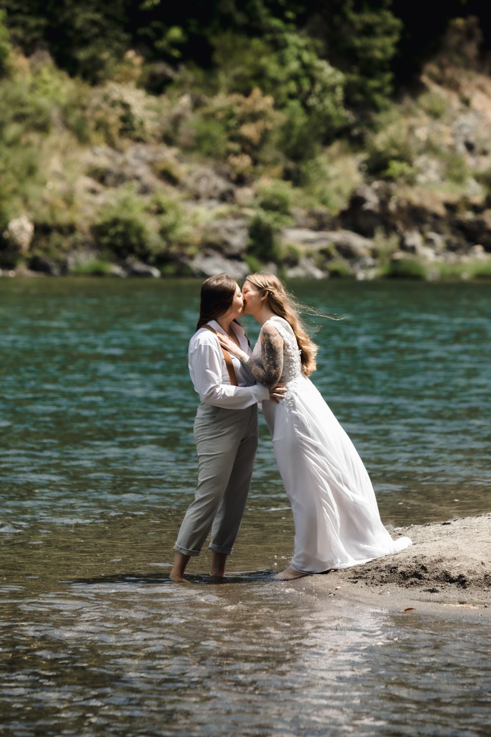 Gay couple kisses while standing in a turquoise river on their wedding day