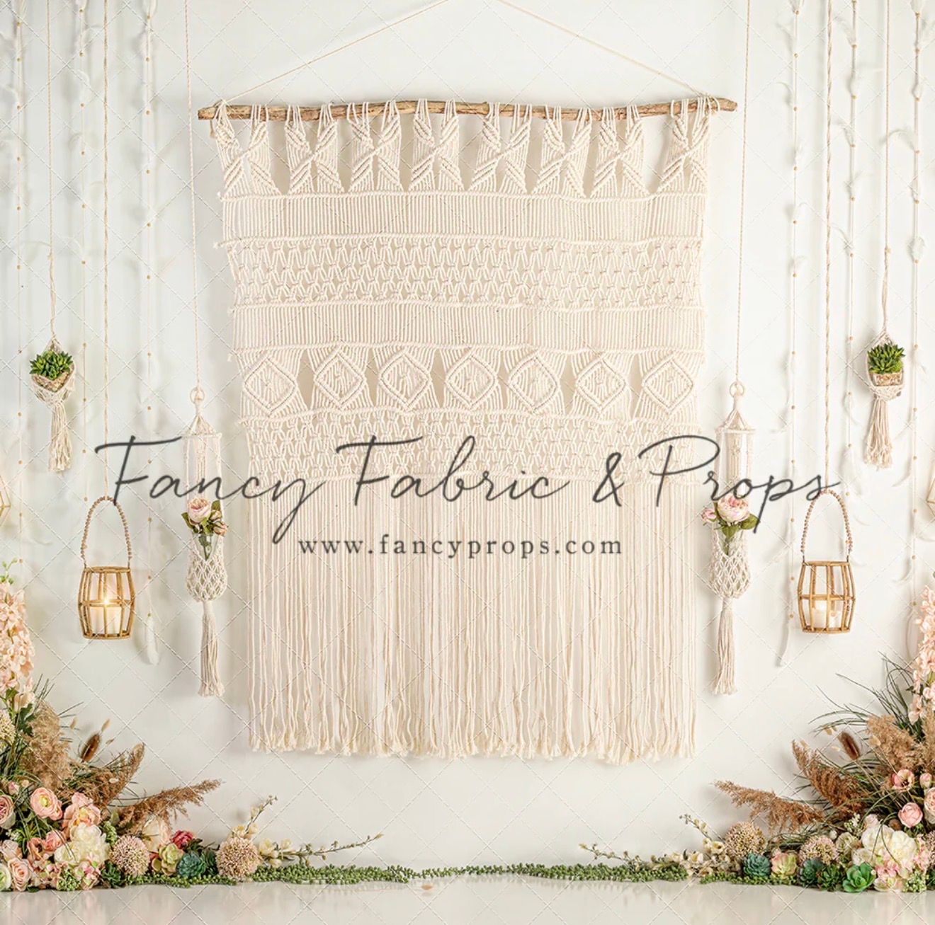 Boho macrame wall hanging backdrop with fringe, lanterns, and floral arrangements by Fancy Fabric & Props.