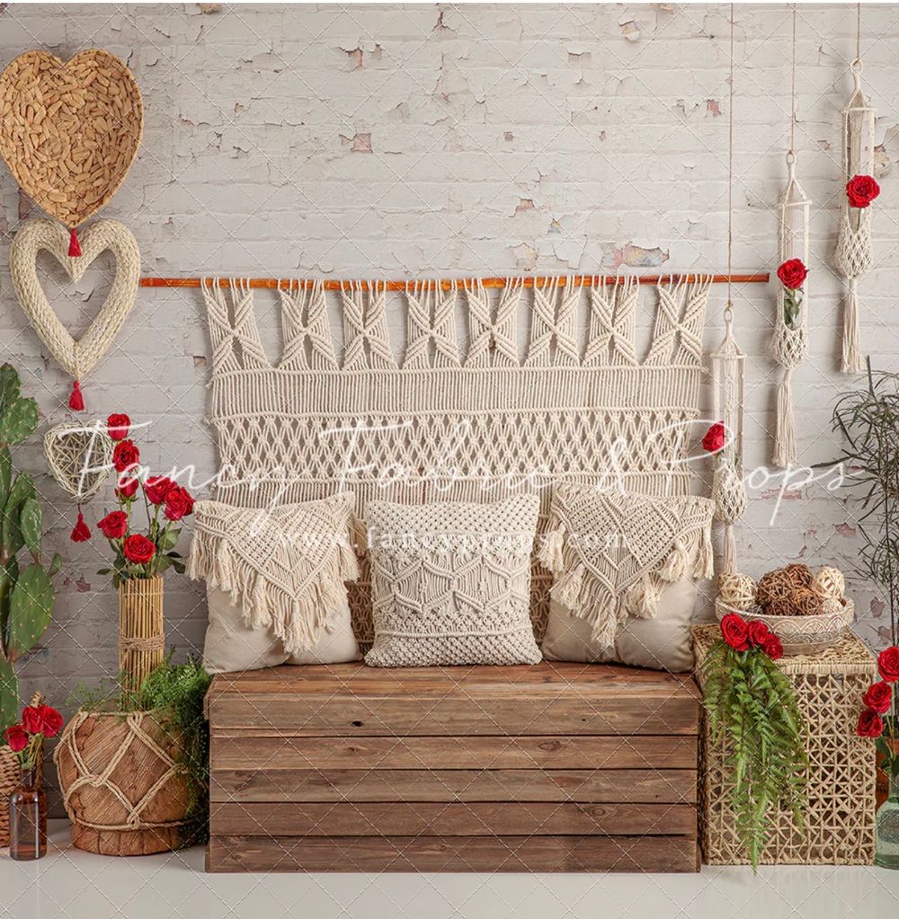 Rustic wooden bench with macrame wall hanging, boho pillows, red roses, wicker baskets, and heart decor on white brick wall.