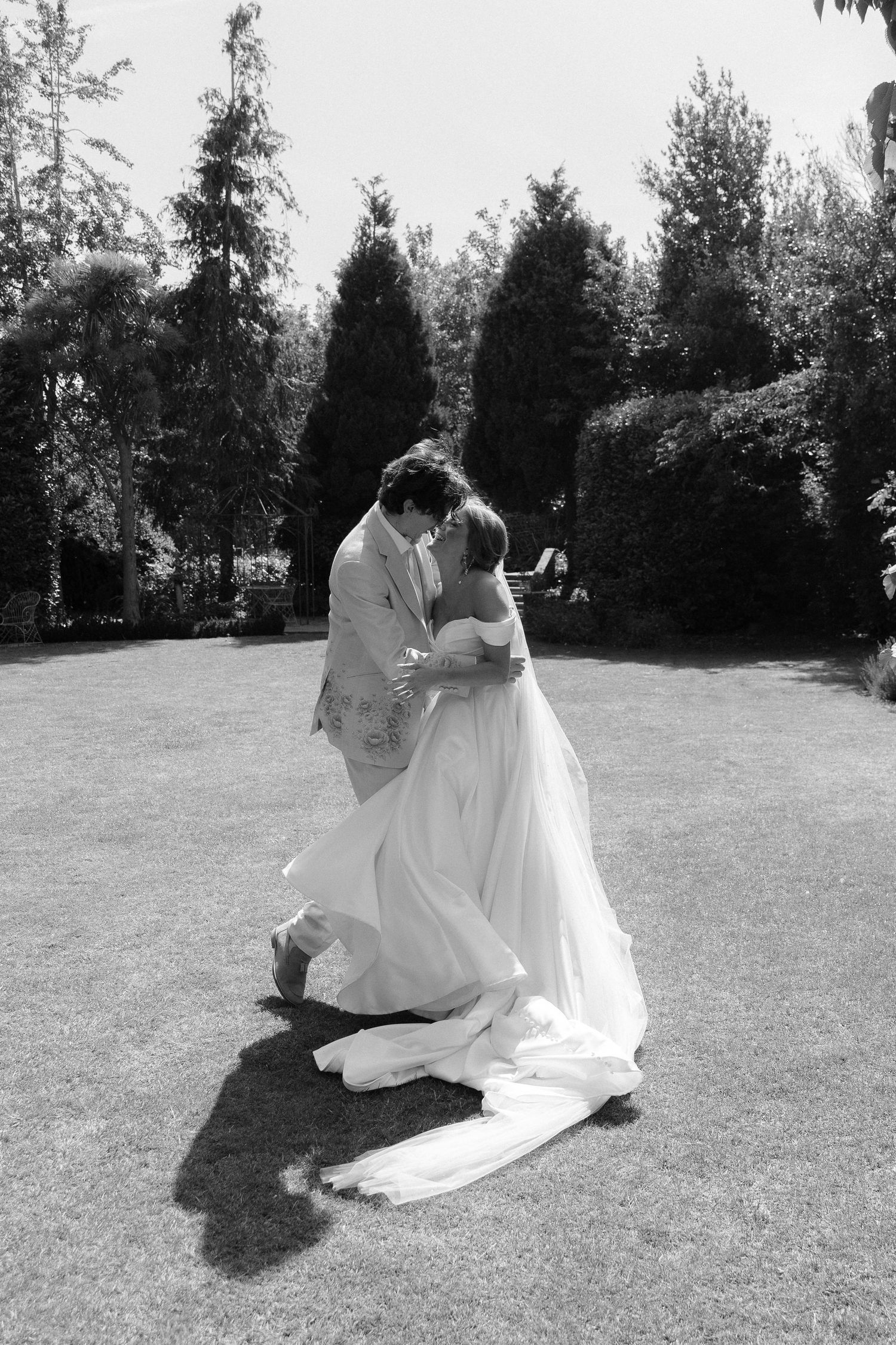 Black and white photo of a bride laughing at her wedding reception table, wearing a veil and elegant dress.