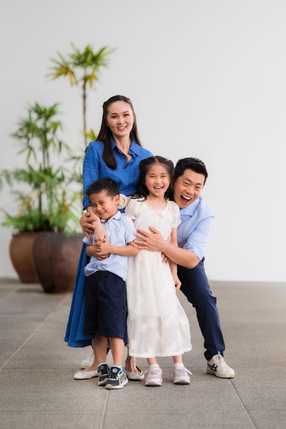Happy Asian family of four posing together outdoors, parents hugging children, smiling joyfully in casual attire.
