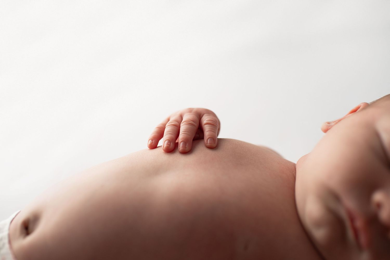 Close-up of a sleeping newborn baby's tiny hand resting on their belly.