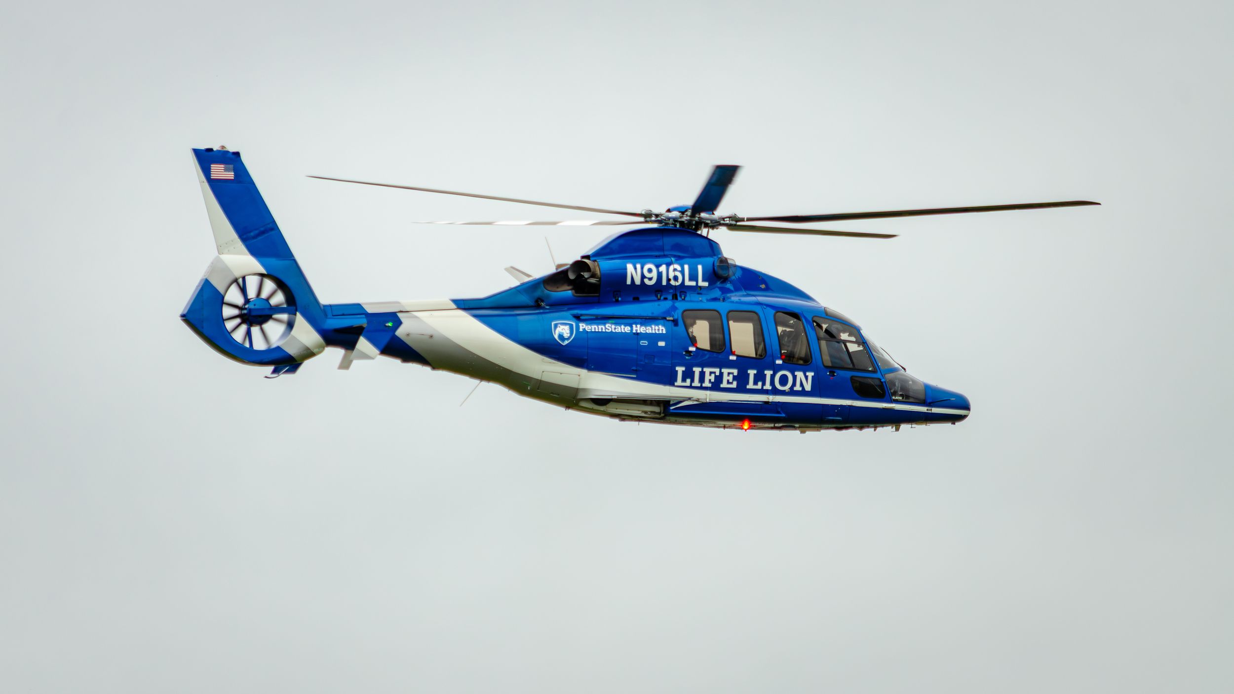Blue and white Life Lion medical helicopter N915LL in flight against overcast sky.