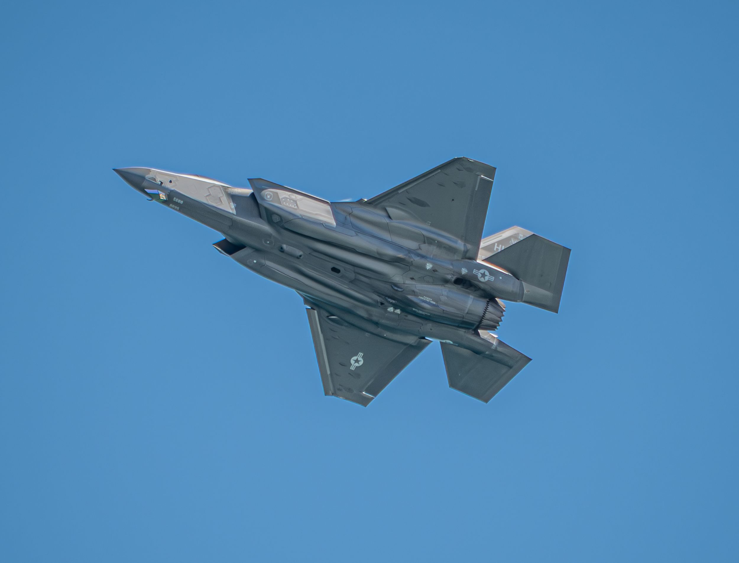 An F-35 stealth fighter jet flying against a clear blue sky, showcasing its advanced aerodynamic design.