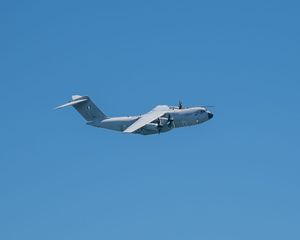 Military cargo aircraft flying against a clear blue sky, showcasing a large gray transport plane in flight.