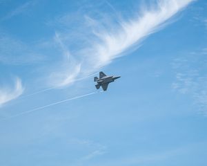 F-35 fighter jet performing aerial maneuver against blue sky with wispy white clouds and contrails.