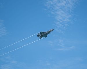 A military jet fighter aircraft flying at high speed against a blue sky, leaving white contrails in its wake.