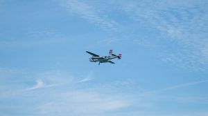 A vintage twin-engine propeller aircraft soaring through a partly cloudy blue sky during an airshow.