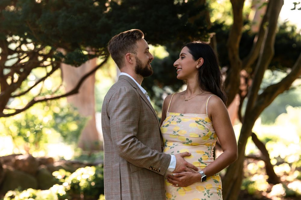 Couple in garden, man in gray suit, woman in yellow floral dress, sharing a romantic moment outdoors.