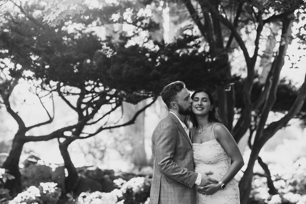 Black and white photo of a couple embracing and kissing among blooming trees in a romantic outdoor setting.