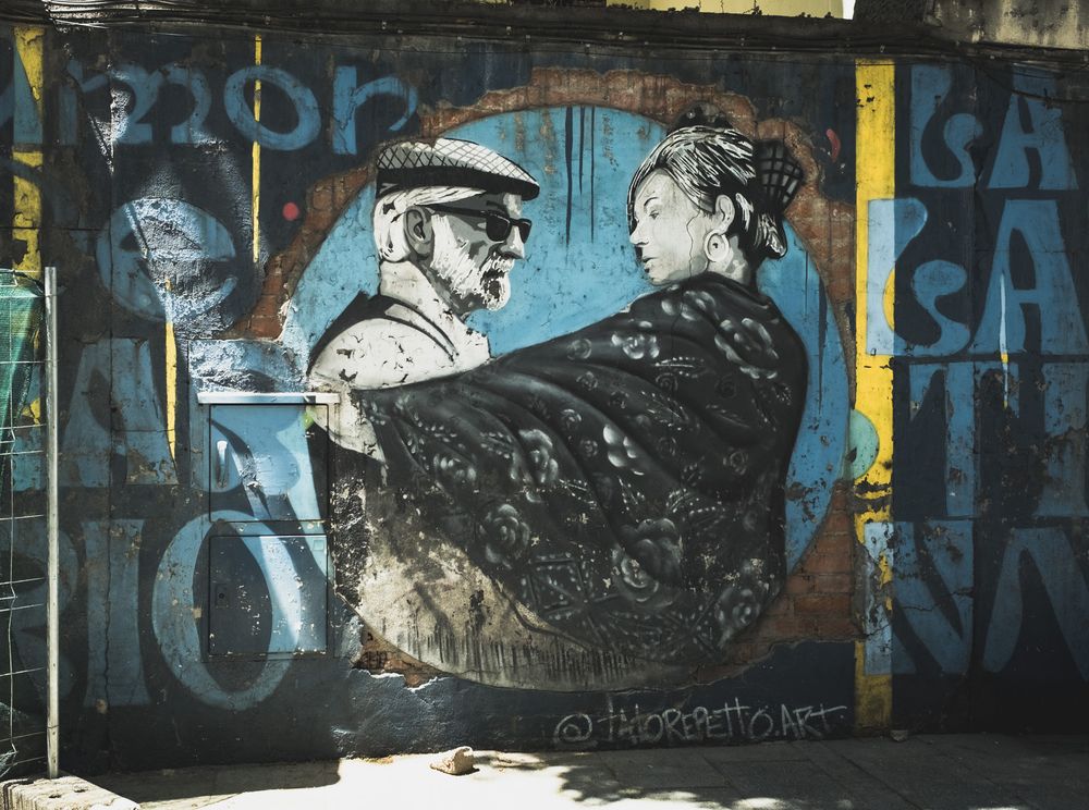 Street art mural depicting elderly couple dancing chotis in traditional Madrid attire on urban wall.