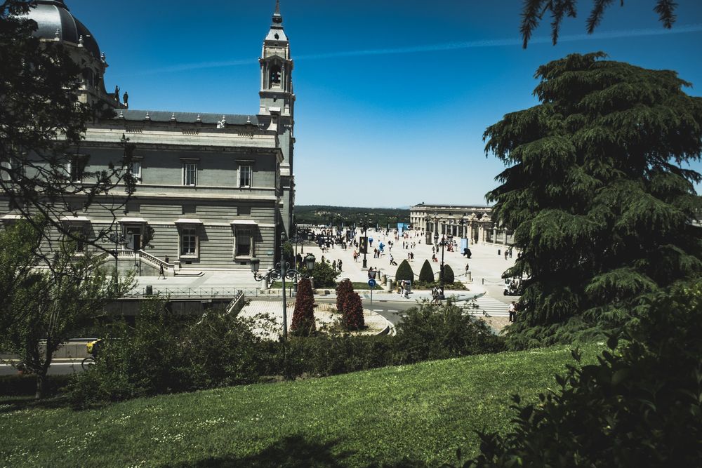 Panoramic view of historic Spanish palace and manicured gardens under bright blue summer sky.