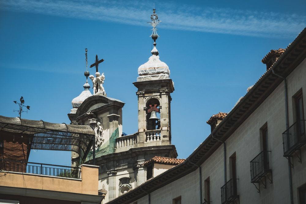 Historic baroque church tower with cross and bell tower against a bright blue sky in Italy.