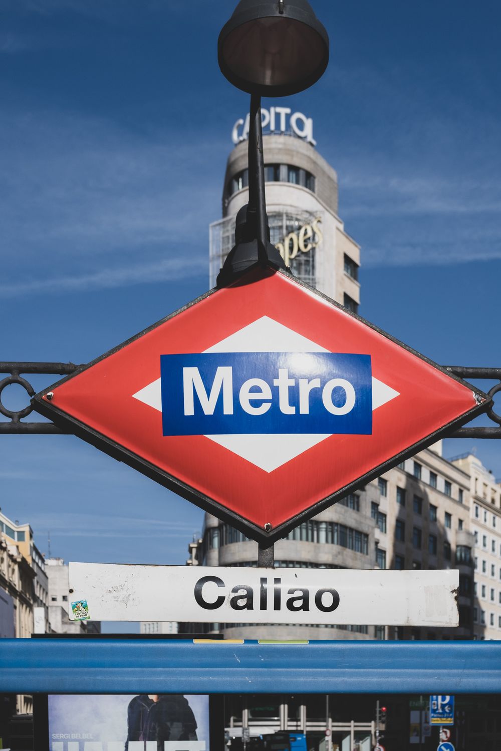 Madrid Metro Callao station sign with the iconic red diamond logo and Edificio Carrion in background.