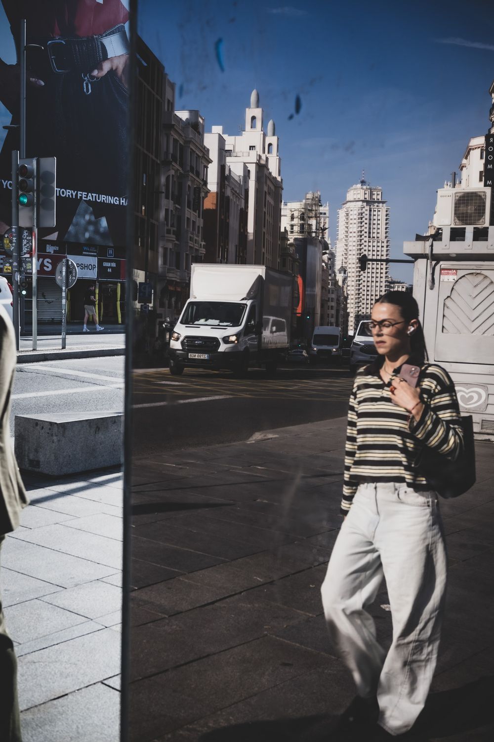 Woman in striped sweater and white jeans standing on a busy urban street with city buildings in background.