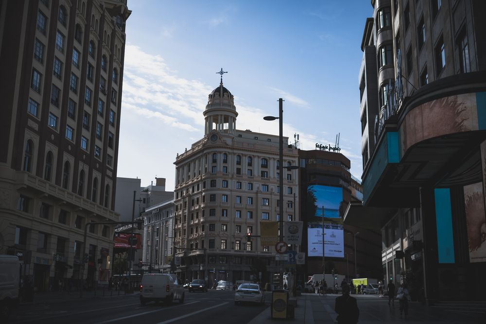 Urban street scene at dusk with historic buildings and illuminated signs in Madrid city center.
