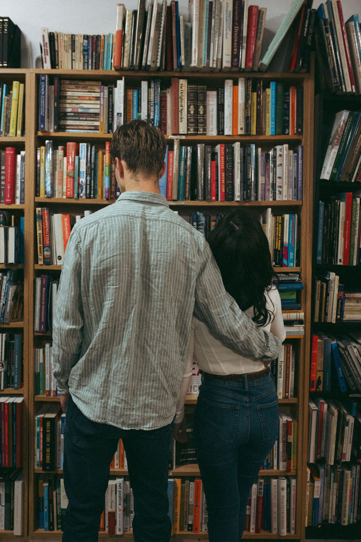 Couple browsing books together at a large wooden bookshelf in a bookstore.