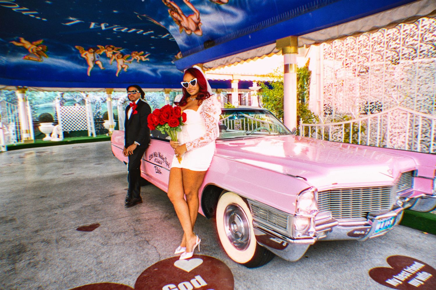 Couple in a black convertible sports car at sunset with mountains in the background, woman's legs resting on the door.